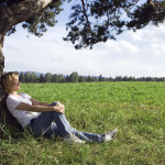 young beauty woman sit under alone tree in field